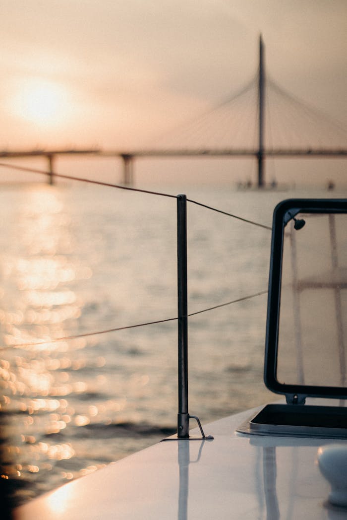 A peaceful sailing scene at sunset with a bridge in the background, reflecting in calm waters.
